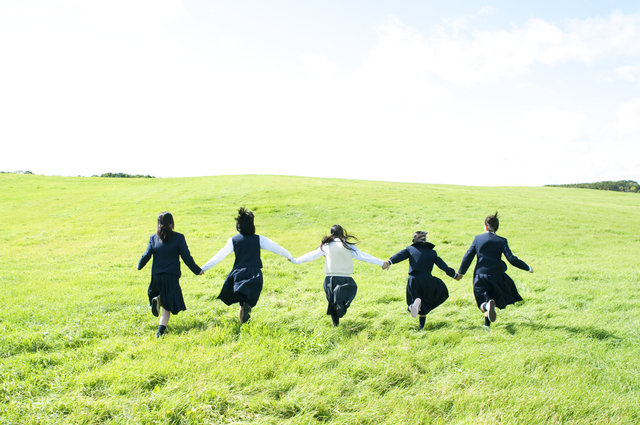 草原で手をつなぎ走る中学生たち