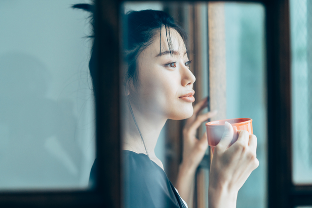 朝に窓際でコーヒーを飲む女性