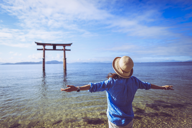 湖と鳥居を見つめる女性旅行者