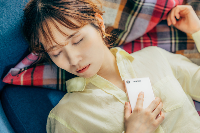 携帯電話を持ちながら寝る女性