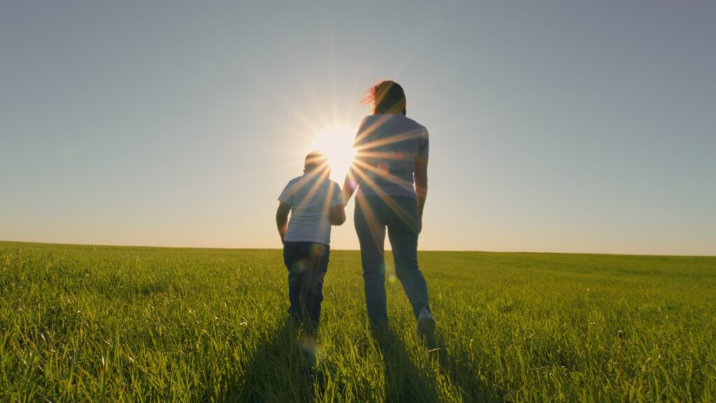 Happy Family Mom Parent And Son Kid Child Going Together. Healthy Lifestyle. Mother And Son Friendly Family. People Enjoying Nature Around Green Grass. Gimbal Stabilize.