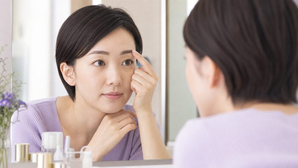 鏡を見ながら眉毛の1本の白い毛に気づく日本人女性